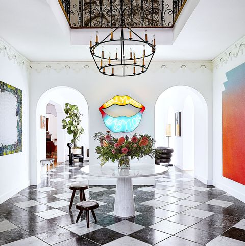 large open entry area with a white round table with flowers on it small stools and neon set of lips on the wall between archways and a black and white floor