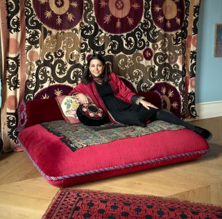 carolina vincenti in her bedroom, on a cushion covered in an antique handwoven romanian skirt and a wall tapestry behind her