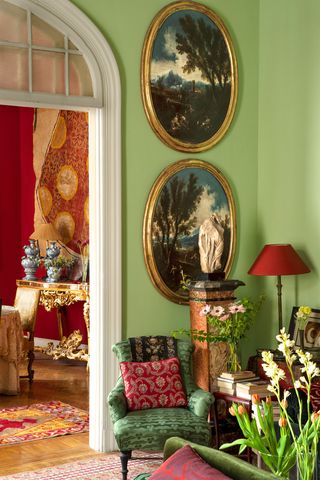 sitting area with green silk chair and red linen pillow, marble pedestal with roman sculpture and 17th century landscape on wall, chinese floor lamp with red shade
