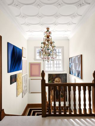 a stairwell with timber balustrade, murano glass chandelier hanging from a decorative ceiling, multiple artworks, and windows letting in natural light