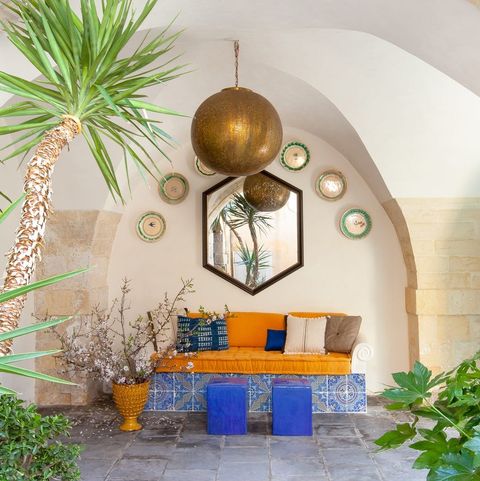 covered outdoor area with orange daybed and bright blue stools and a mirror above and a semi circle of plates and giant orb hanging at center