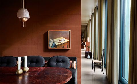 a spice color paneled wall carves out the dining room in the loftlike apartment, a brass and glass pendant descends over the wood table and dark blue banquette, behind which hangs a still life painting