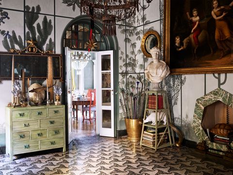 the entryway has a patterned marble floor, an antique chest of drawers with art objects on top, a stand with a marble bust of africa, a heptagonal fireplace, and an antique tin chandelier.