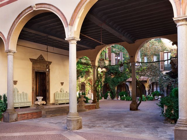 an italian courtyard with arches and columns, two benches flanking a decorative doorway, greenery climbing walls in the background
