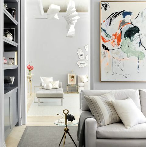 white living area with sofa and cusions and small tripod table next to you looking into another room with a off white chaise lounge and other sofas