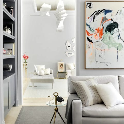 white living area with sofa and cusions and small tripod table next to you looking into another room with a off white chaise lounge and other sofas