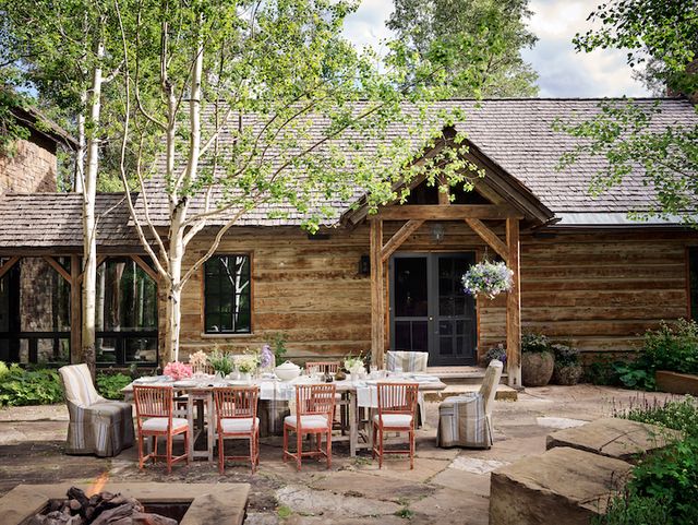 jeffrey bilhuber dining chairs on a stone patio in front of a rustic log house