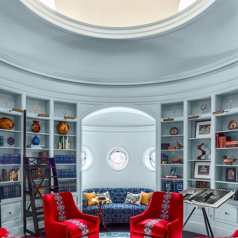 round room with four bright red velvet chairs in a circle around a small table shaped like a spool with chess board on it and a blue tufted banquette tucked into the far wall