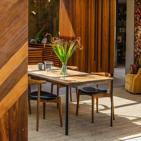 A List 2022 - ELLE DECOR wooden table on a sisal rug in an open room with wooden textured walls