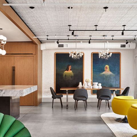 open living area with bright yellow chairs in the foreground and dining table at the far end with two floor to ceiling portraits hanging on the wall behind