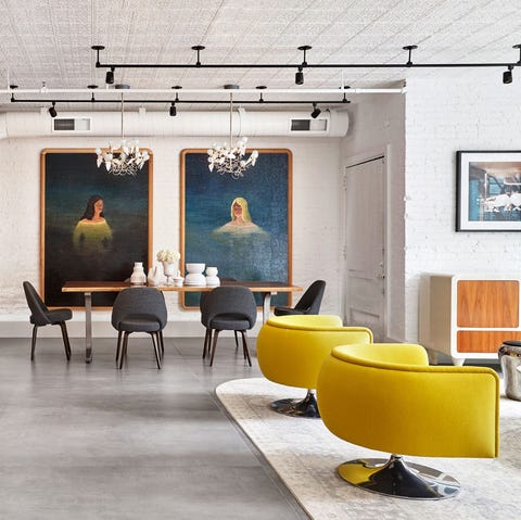 A List 2022 - ELLE DECOR open living area with bright yellow chairs in the foreground and dining table at the far end with two floor to ceiling portraits hanging on the wall behind
