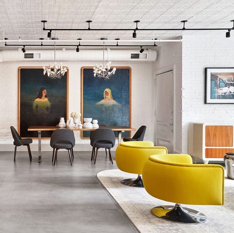 open living area with bright yellow chairs in the foreground and dining table at the far end with two floor to ceiling portraits hanging on the wall behind