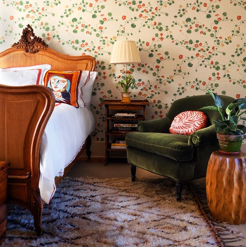 A List 2022 - ELLE DECOR bedroom with viney green and red flowered wallpaper a sleigh bed and a green velvet upholstered chair to the right