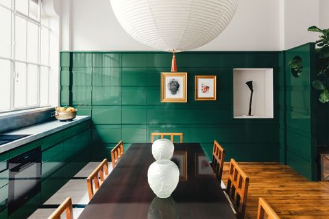 minimalist kitchen with long wood table in the center and green lacquered cabinets the left and green tiled half wall all around large round pendant light hangs down over the table