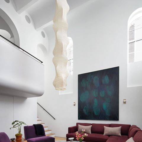 living area with high ceilings wraparound sofa in dark burgundy with armless chairs in complimentary dark purple velvet and a low coffee table with triangular pedestal and large handing pendant from ceiling