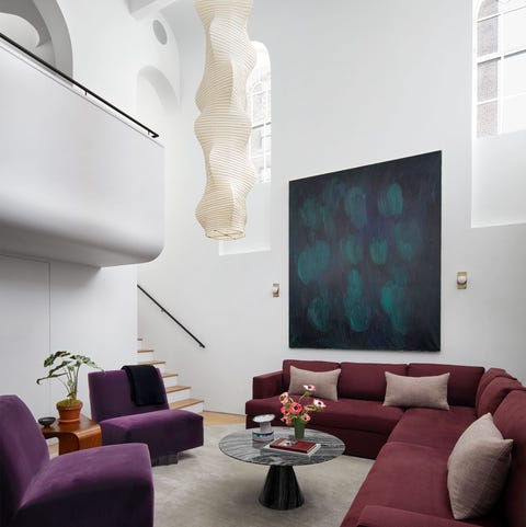 living area with high ceilings wraparound sofa in dark burgundy with armless chairs in complimentary dark purple velvet and a low coffee table with triangular pedestal and large handing pendant from ceiling