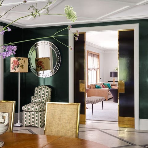 dark blue wall with round mirror flanking a doorway and a table and gold trimmed chairs in the foreground