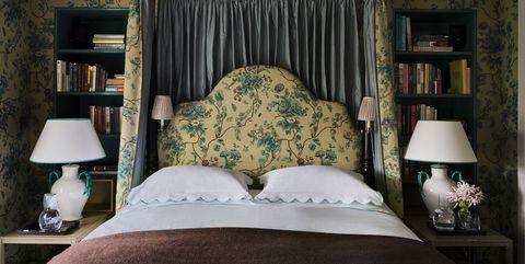 walls, bed curtains and headboard are in a fabric with a green floral pattern on a light yellow background, sconces are attached to headboard, side tables with lamps, and bed is flanked by bookshelves