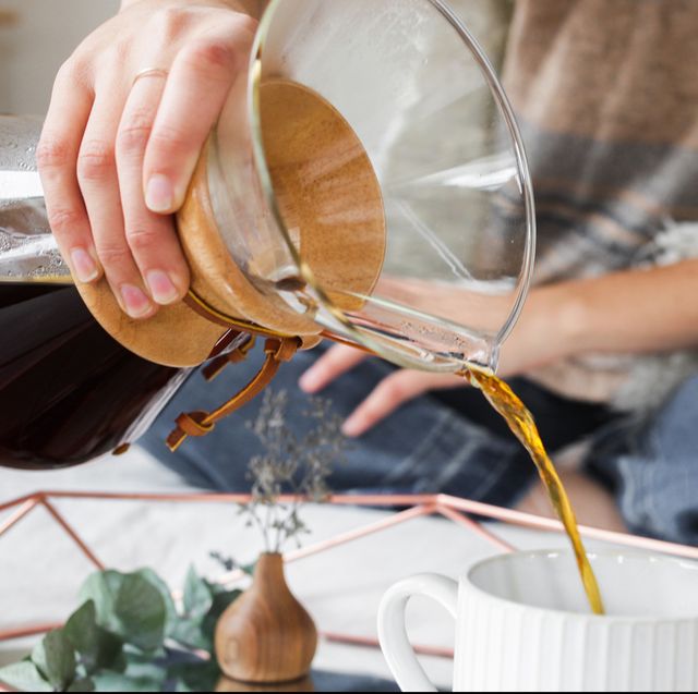 woman pouring Chemex coffee into mug while sitting on bed 