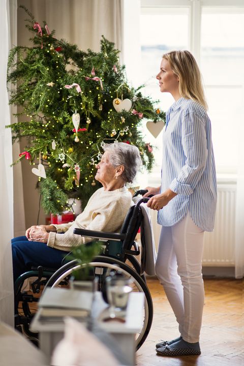 a senior woman in wheelchair with a health visitor at home at christmas time, looking out of a window