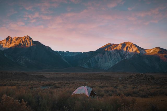 camping in field by mountains as sun rises