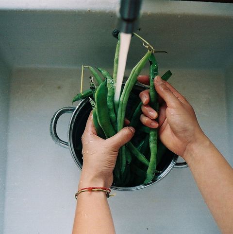 manos de mujer lavando unas judías verdes bajo el grifo
