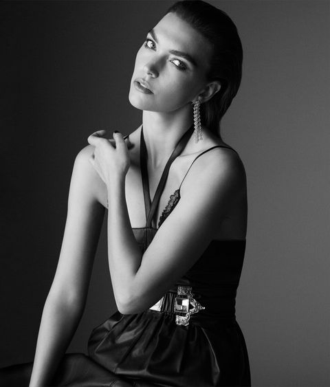 arizona muse wears a black halter necked dress with a belt and earrings