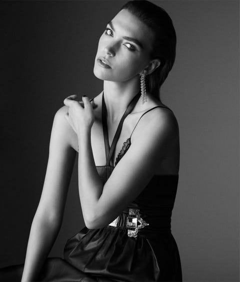 arizona muse wears a black halter necked dress with a belt and earrings