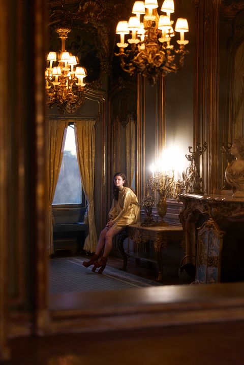 alison oliver sits against a desk in an ornate house
