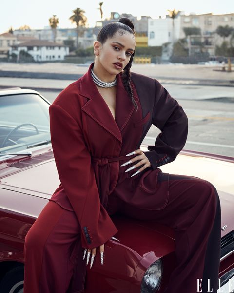 rosalía in red suit sits on car