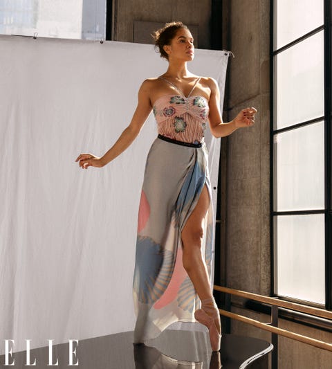 misty copeland stands en pointe atop a piano in an airy studio wearing a pink, blue, and gray dress with flower details