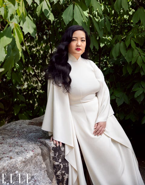 amanda nguyen rests against a rock wearing a white ao da