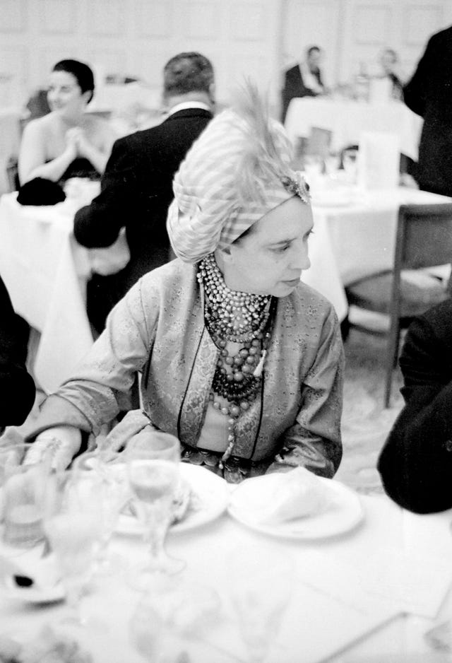 French-born Italian fashion designer Elsa Schiaparelli 1890 1973 wearing a turban with a single feather as she sits at the dinner table for a formal occasion, 1940 photograph from the Roger Viollet collection