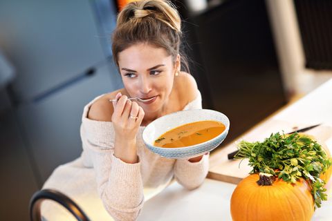 Adult woman eating pumpkin soup in the kitchen