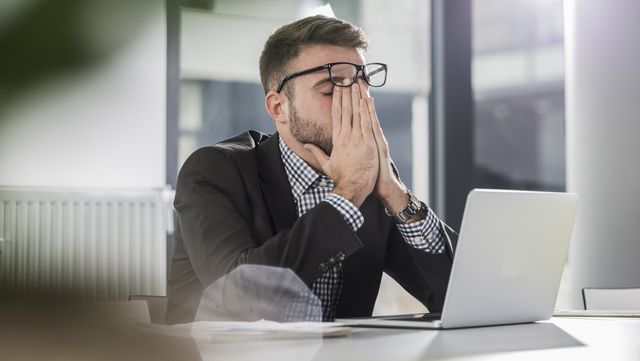 exhausted young man with laptop in office
