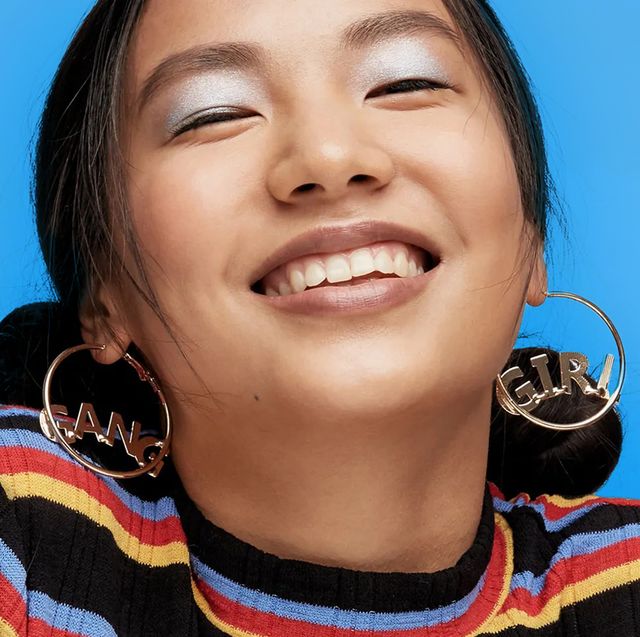 girl with large hoop earings and shimmery blue eyeshadow smiling