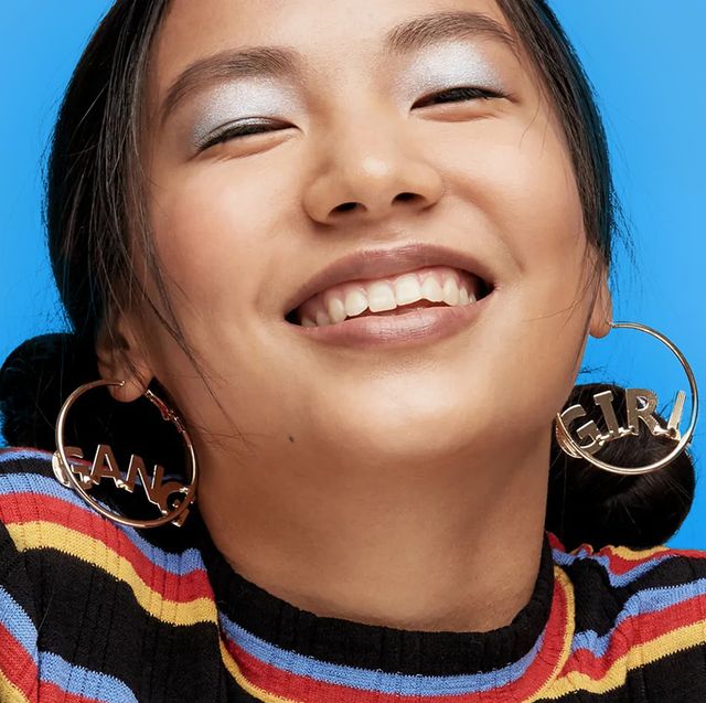 girl with large hoop earings and shimmery blue eyeshadow smiling