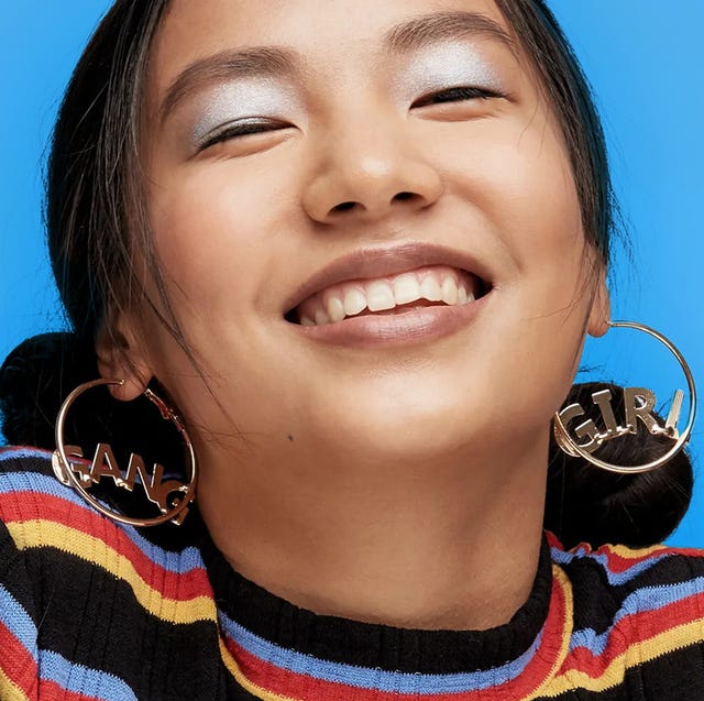 girl with large hoop earings and shimmery blue eyeshadow smiling