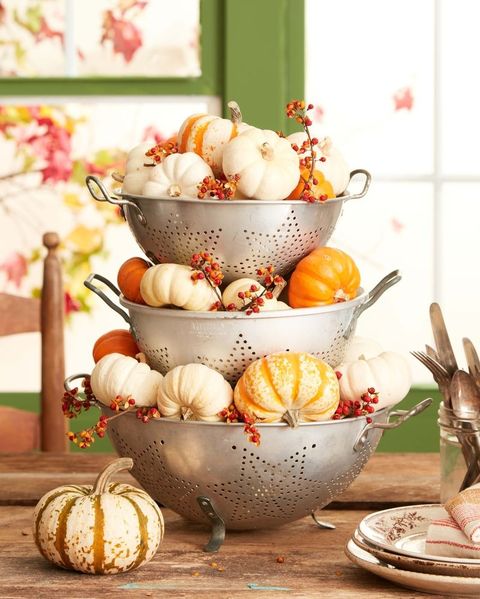 small white, orange, and striped pumpkins displayed in stacked vintage colanders with small sprigs of bittersweet poking in