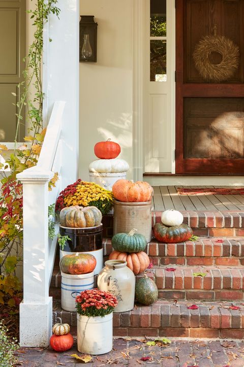 pumpkins and mums in vintage crocks arranged on brick steps along chunky white wood railing leading to a covered front porch