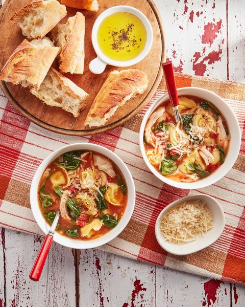 chicken and spinach tortellini soup in two bowls with a wooden board of bread next to them and a small bowl of parmesan cheese for serving
