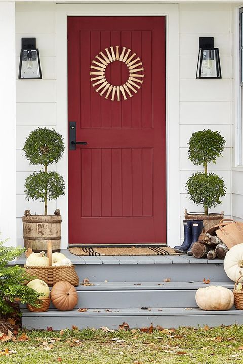 handmade shaker peg wreath on red door on a front porch decorated with topiaries and fall gourds