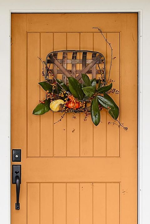 tobacco basket door hanging with magnolia leaves and fake pumpkins on an orange front door