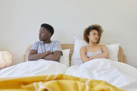 falling out of love couple sitting in bed under covers not looking at each other with arms crossed