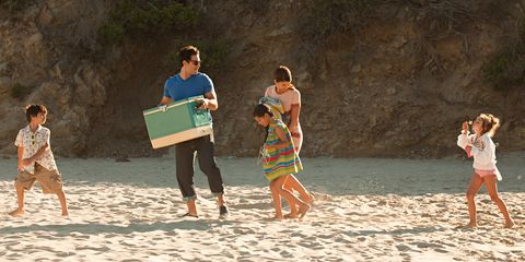 Family on beach, father carrying coolbox