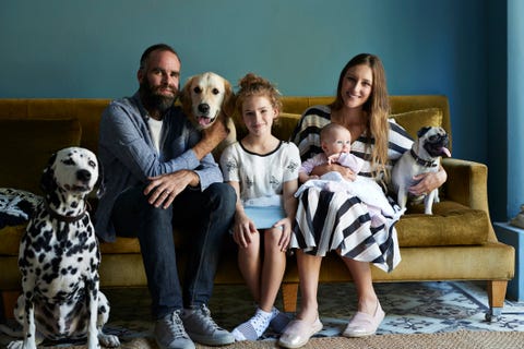 Una familia sentada en su sofá con sus perros un padre, una madre con sus dos hijas y sus tres perros en su salón