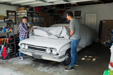 Father and son uncovering vintage car in garage
