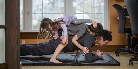 A father holds a plank position with two children piled on his back