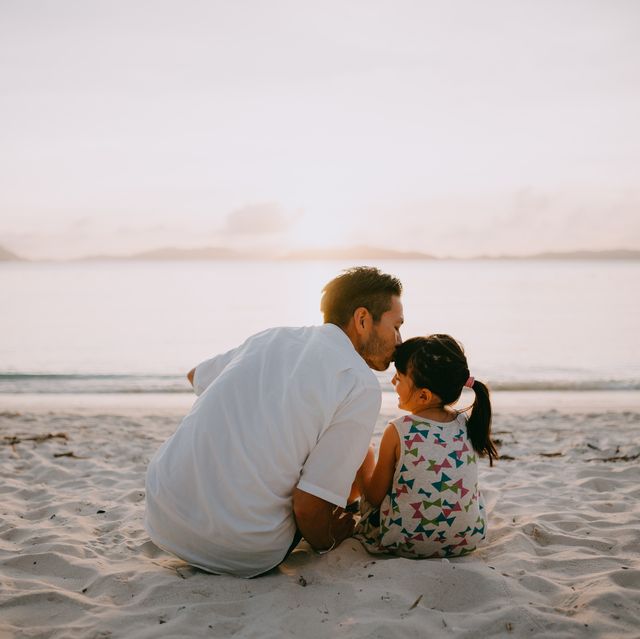 father kissing daughter on beach at sunset, okinawa, japan