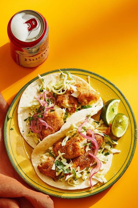 beer battered fish tacos with lime wedges on the side and a can of beer